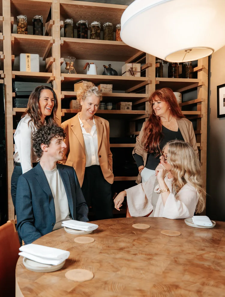 The Buyers Agents team gathered around a table talking and laughing together